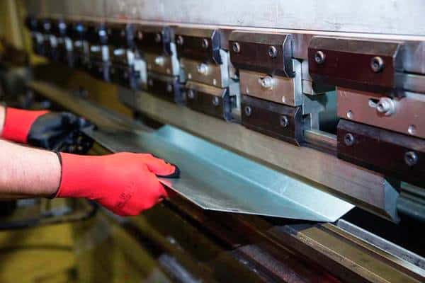 Worker operating metal sheet bending machine with safety gloves.