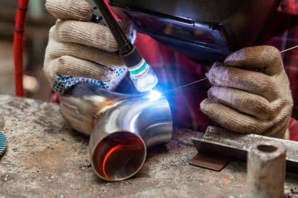 Welder using TIG welding on metal pipe.