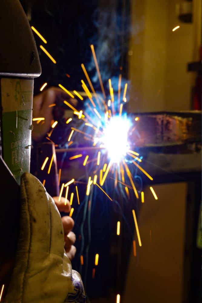 Welder with protective gear welding metal with sparks flying.